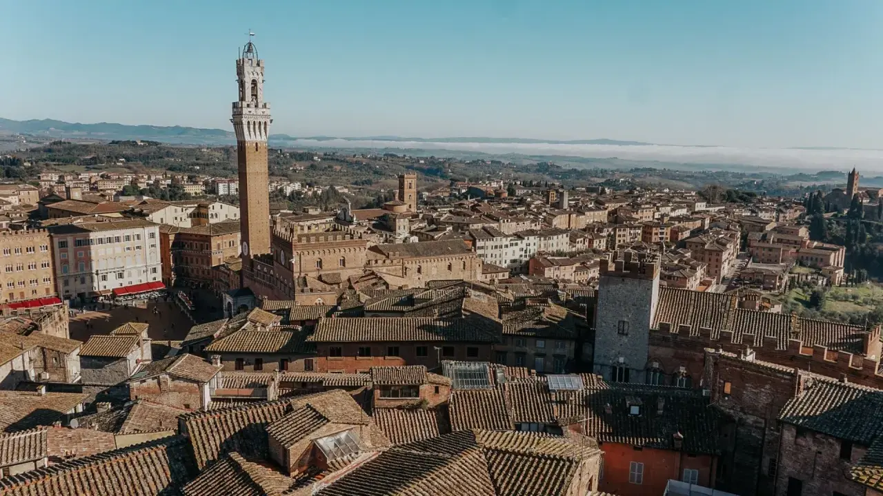 Vista aerea di Siena, con la Torre del Mangia in primo piano. Un'idea per cosa vedere in Toscana in 2 giorni, tra tetti in cotto e colline nebbiose.