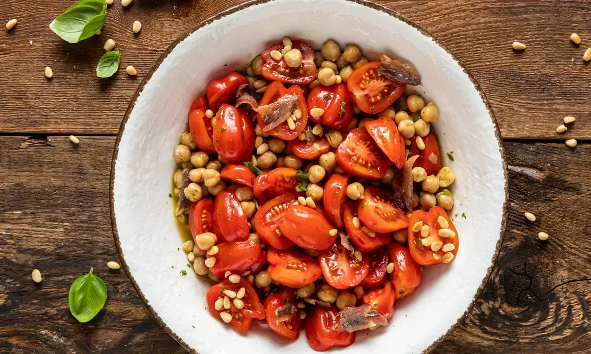 Insalata di ceci e pomodorini, un'idea fresca per le tue ricette con farina di ceci. Guarnita con pinoli e acciughe.