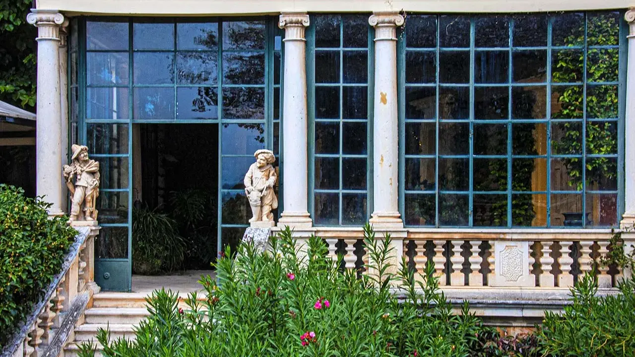 Statue di nani custodi di un giardino lussureggiante sui Colli Berici, con un'elegante serra sullo sfondo.