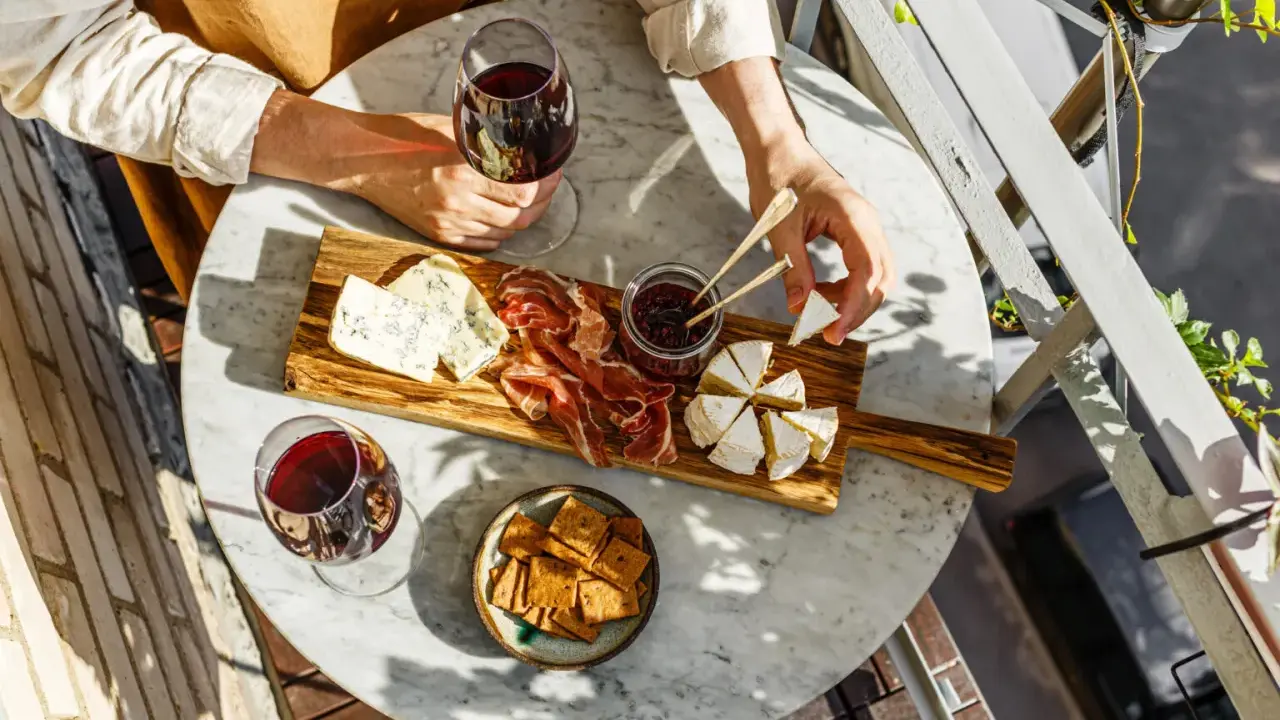 Un tagliere con formaggi, salumi e marmellata, accompagnato da un bicchiere di vino rosso. Le caratteristiche del nebbiolo vino si esaltano con questi sapori.