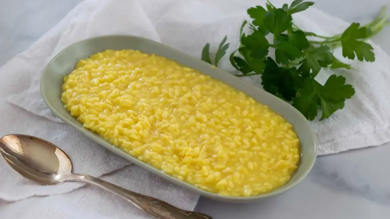 Un cremoso risotto al pistacchio, servito in un piatto ovale con un cucchiaio d'argento e un rametto di prezzemolo fresco.