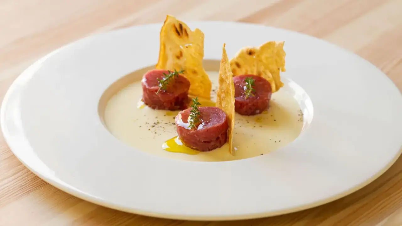 Tre cilindri di tartare di manzo, guarniti con timo, su una crema chiara e croccanti cialde. Un'idea su come condirla.