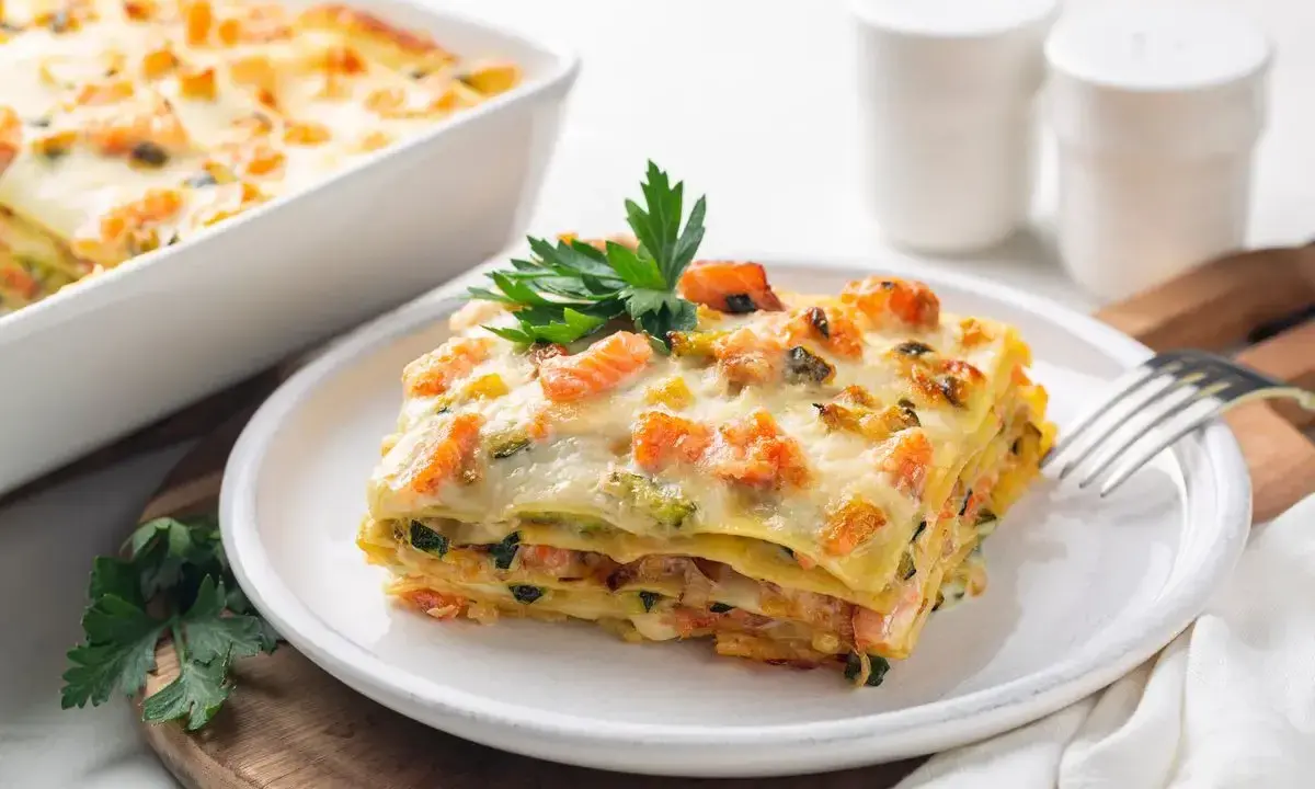 Una fetta di lasagne di pesce, stratificata con salmone e zucchine, guarnita con prezzemolo.