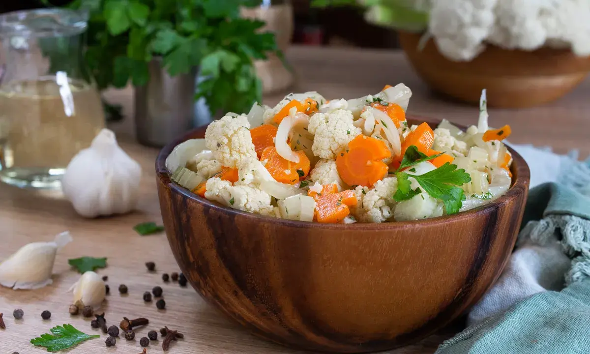 Un'appetitosa giardiniera in agrodolce, con cavolfiore, carote e cipolle, servita in una ciotola di legno.