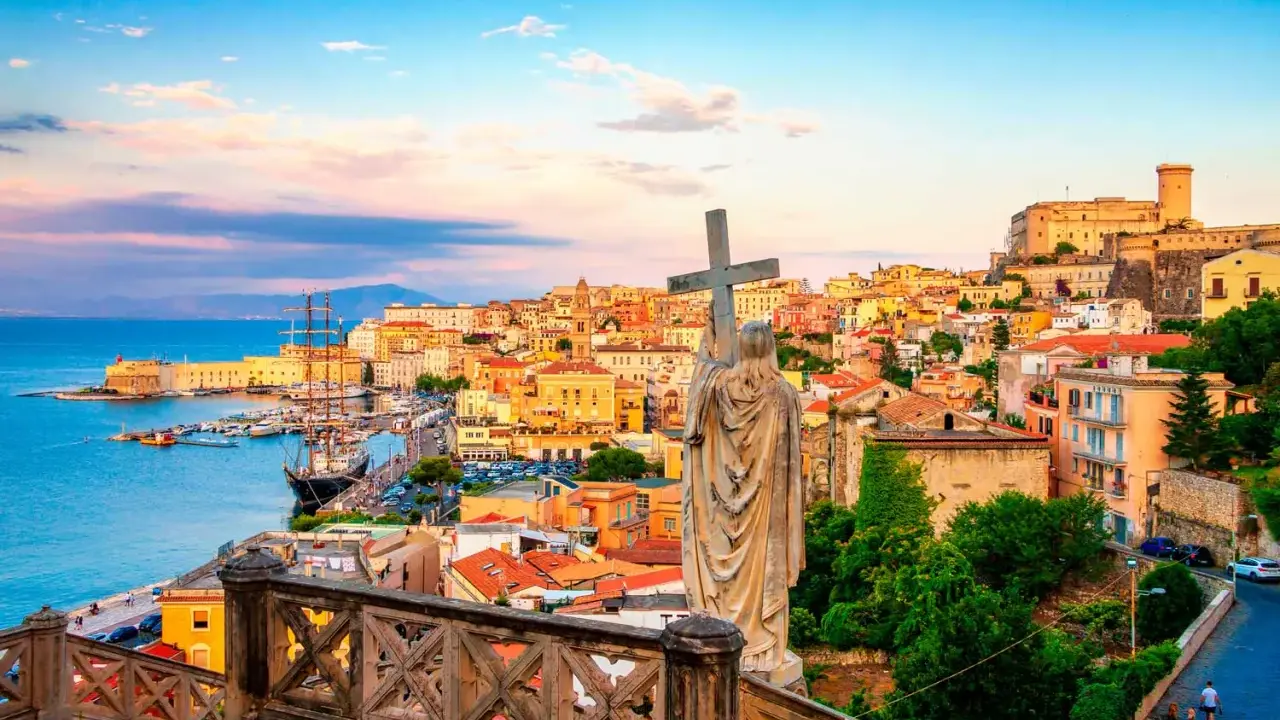 Statua con croce domina la vista di Gaeta, perfetta per una gita fuori porta da Roma. Porto, case colorate e castello sullo sfondo.