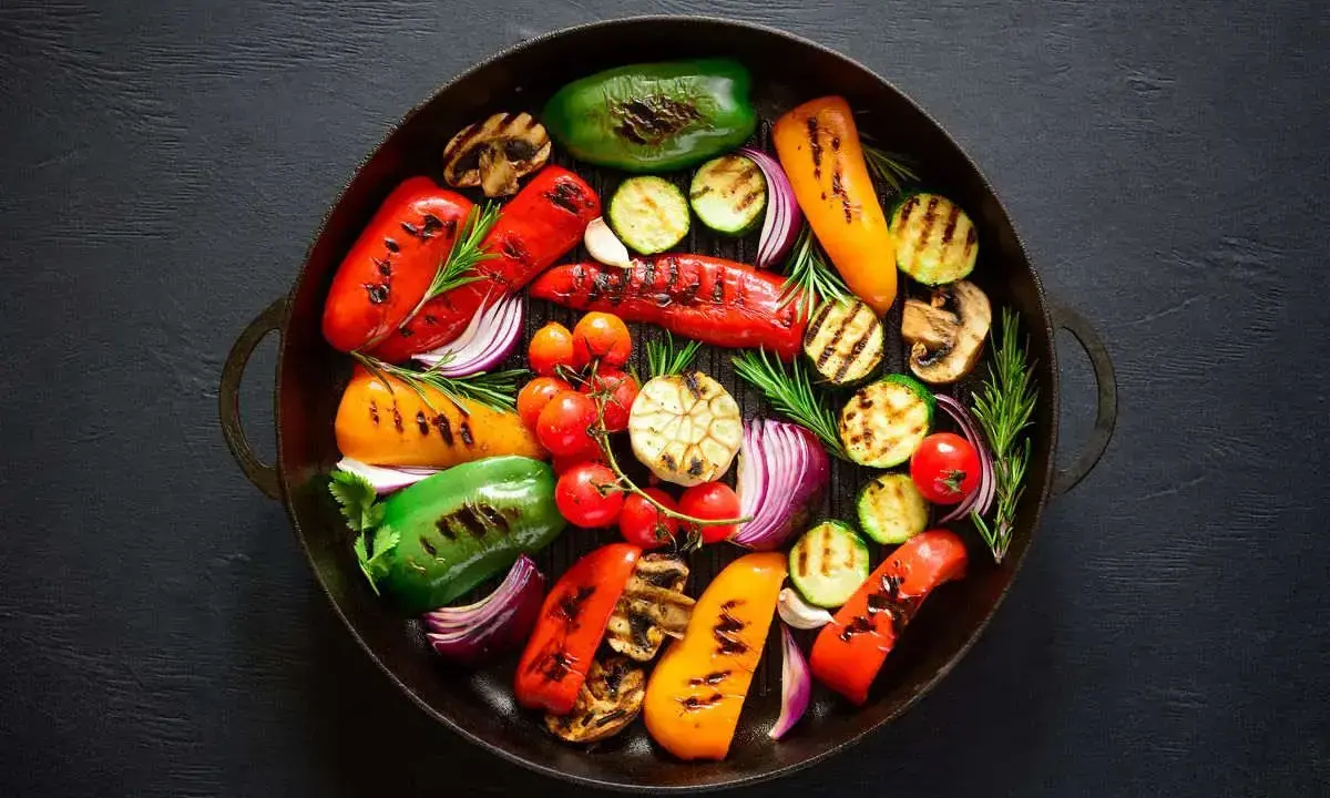 Un assortimento colorato di verdure grigliate, tra cui peperoni, zucchine, cipolle rosse e pomodorini, disposte in una padella di ghisa.