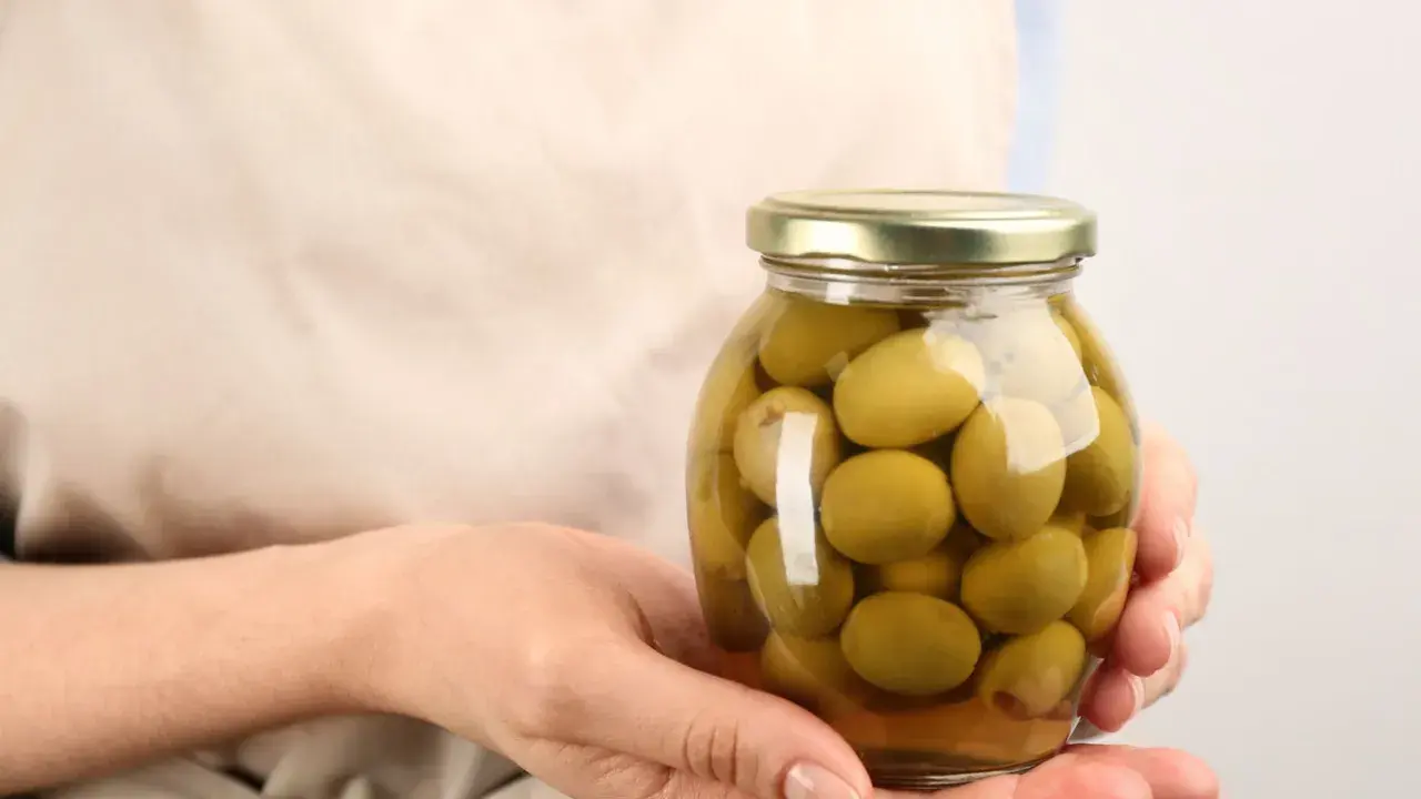 Mani che tengono un barattolo di olive verdi in salamoia per olive, pronte per essere gustate.