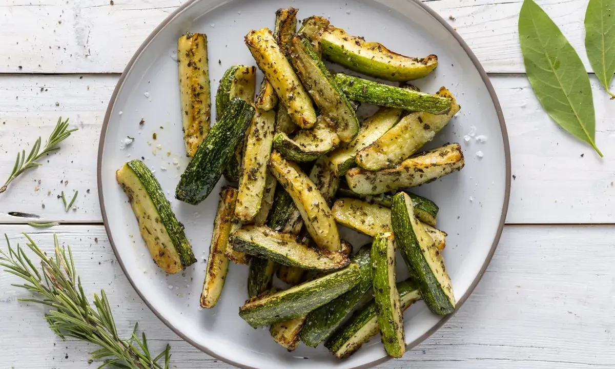 Zucchine in friggitrice ad aria, tagliate a bastoncini e condite con erbe aromatiche, pronte per essere gustate.