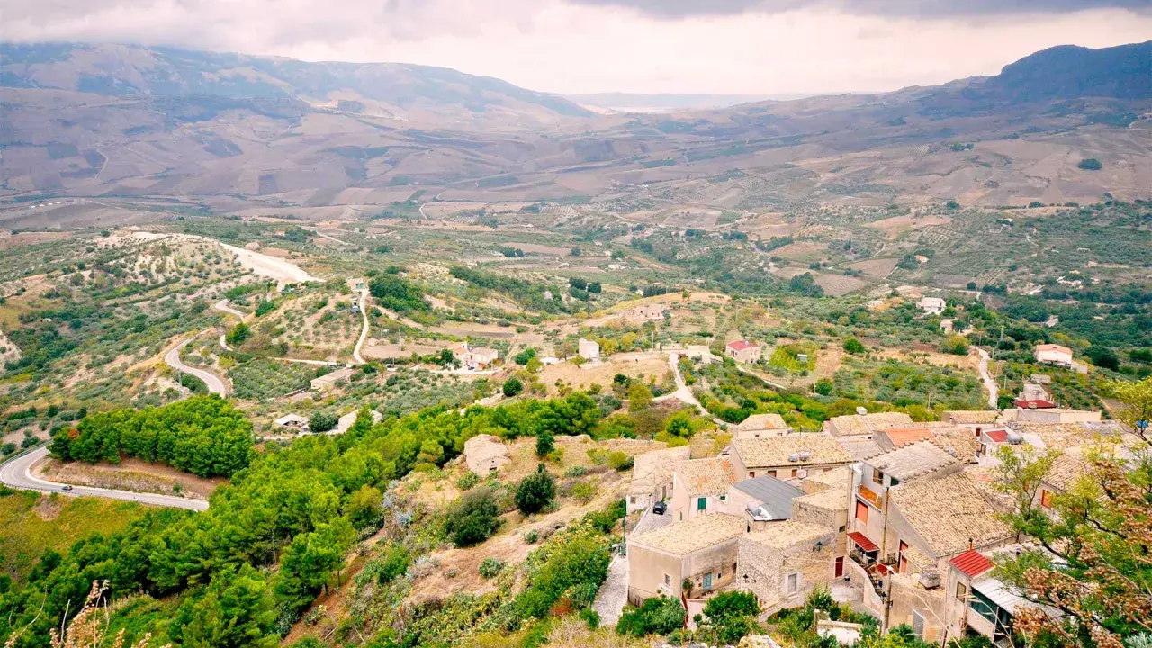 Panoramica di Contessa Entellina, un borgo siciliano tra colline verdi e campi coltivati, con case dai tetti in cotto e una strada tortuosa.