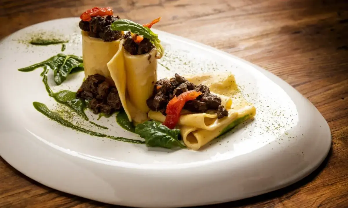 Pappardelle alla lepre, un piatto ricco e saporito, con pasta fresca, ragù scuro e guarnizioni verdi.