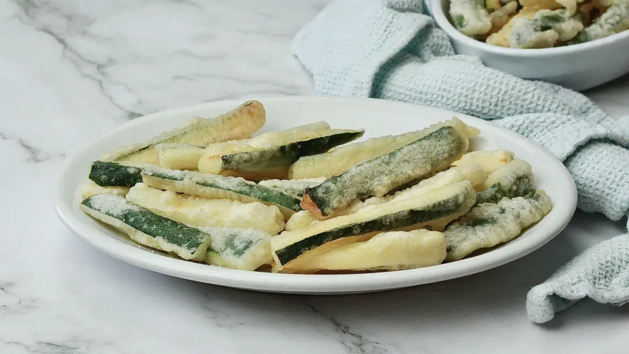 Zucchine fritte in pastella dorata, croccanti e invitanti, servite su un piatto bianco.
