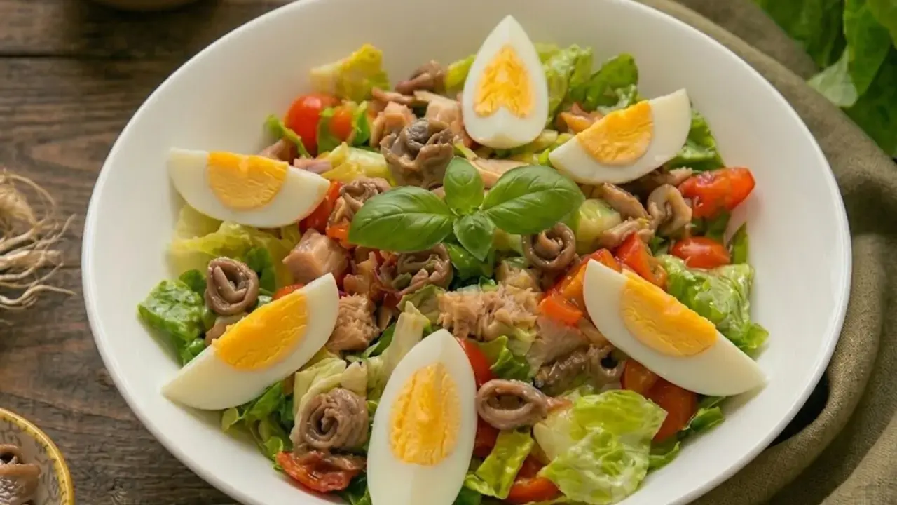 Insalata nizzarda con uova sode, tonno, acciughe, pomodorini e lattuga. Ingredienti freschi per un piatto gustoso.