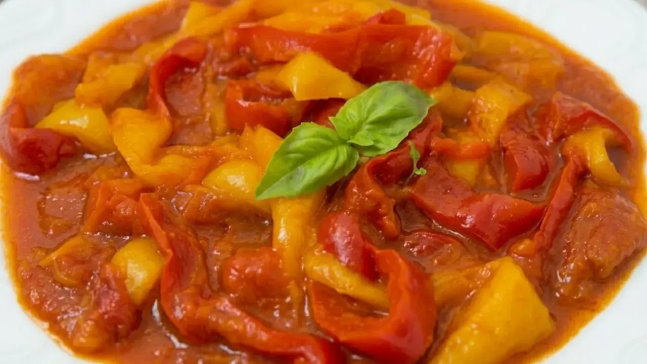 Peperonata ricetta della nonna: peperoni rossi e gialli cotti lentamente in un sugo saporito, guarniti con basilico fresco.
