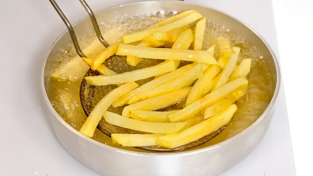 Patate fritte dorate che sfrigolano nell'olio bollente, pronte per essere gustate.