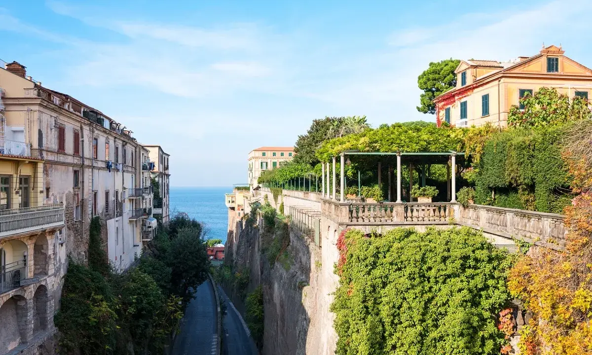 Edifici affacciati sul mare blu, con un viale alberato che scende verso la costa. La **penisola sorrentina** offre scorci mozzafiato tra ville storiche e vegetazione rigogliosa.
