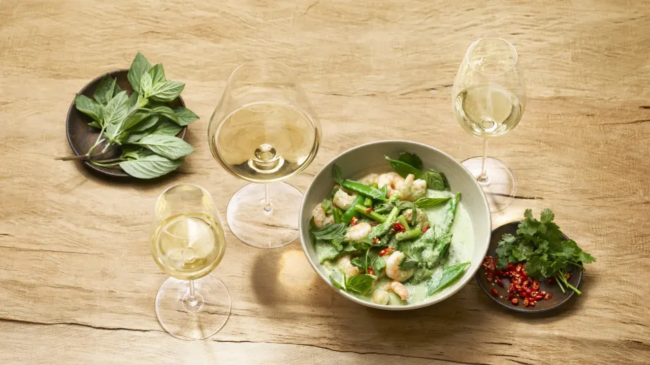 Un curry verde con gamberi e verdure, accompagnato da bicchieri di vino bianco, evoca le fresche **sauvignon blanc caratteristiche**.