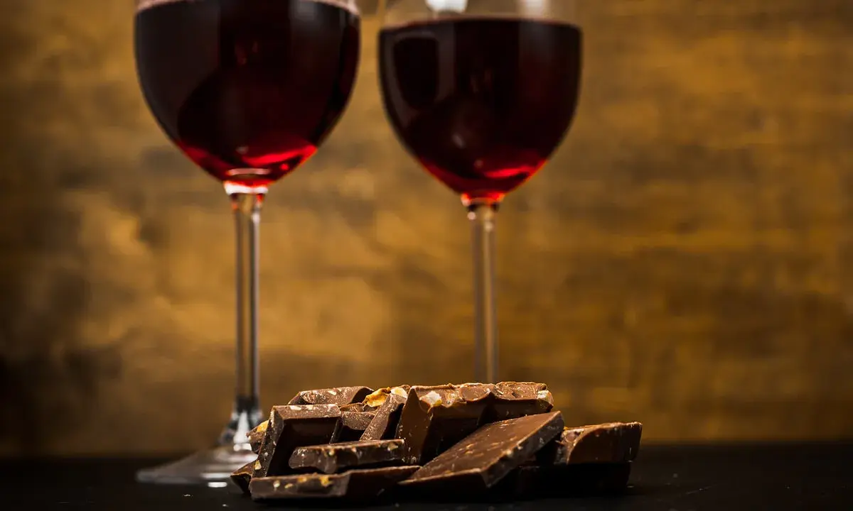 Due calici di vino rosso e una pila di cioccolato fondente, un perfetto abbinamento vino e cioccolato per un momento di piacere.