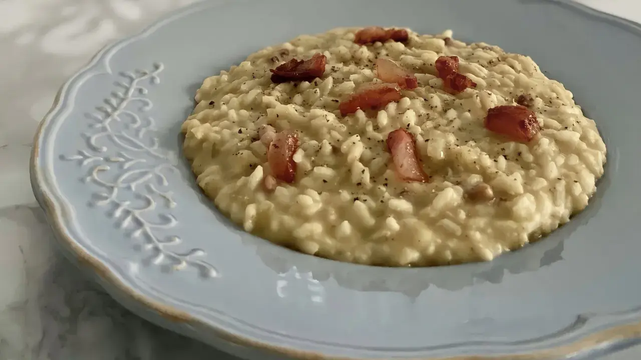 Un cremoso risotto con ceci e pancetta croccante, servito su un piatto azzurro decorato.
