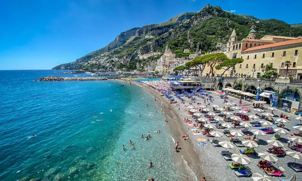 Spiaggia affollata con ombrelloni e gente che nuota in acque cristalline. Un'idea perfetta per decidere dove andare un weekend in Italia.