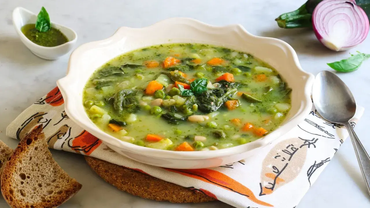 Un fumante minestrone genovese, ricco di verdure fresche, piselli, carote e fagioli, servito con pesto e pane tostato.