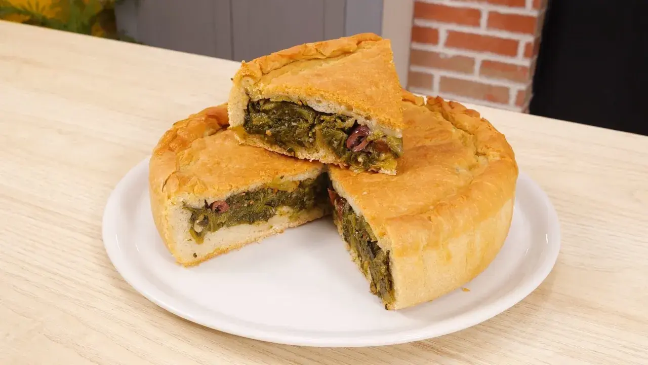 Una fetta di pizza di scarola, ricca di verdure e olive, su un piatto bianco.