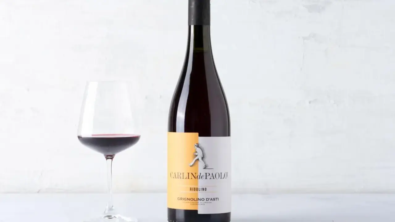 Calice di vino rosso accanto a una bottiglia di Grignolino d'Asti Carlin de Paolo. Un vino che ricorda il barbera vitigno per la sua vivacità.