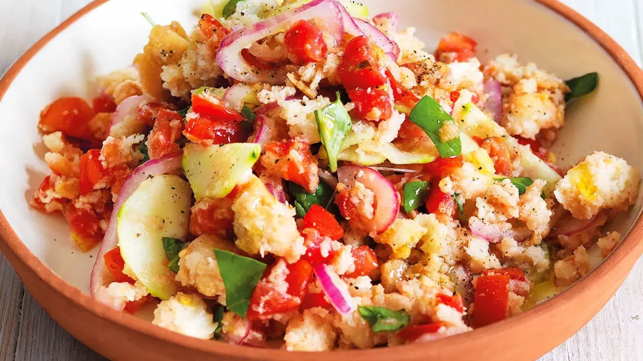 Panzanella ricetta: un'insalata estiva con pane raffermo, pomodori, cetrioli, cipolla rossa e basilico, condita con olio d'oliva.
