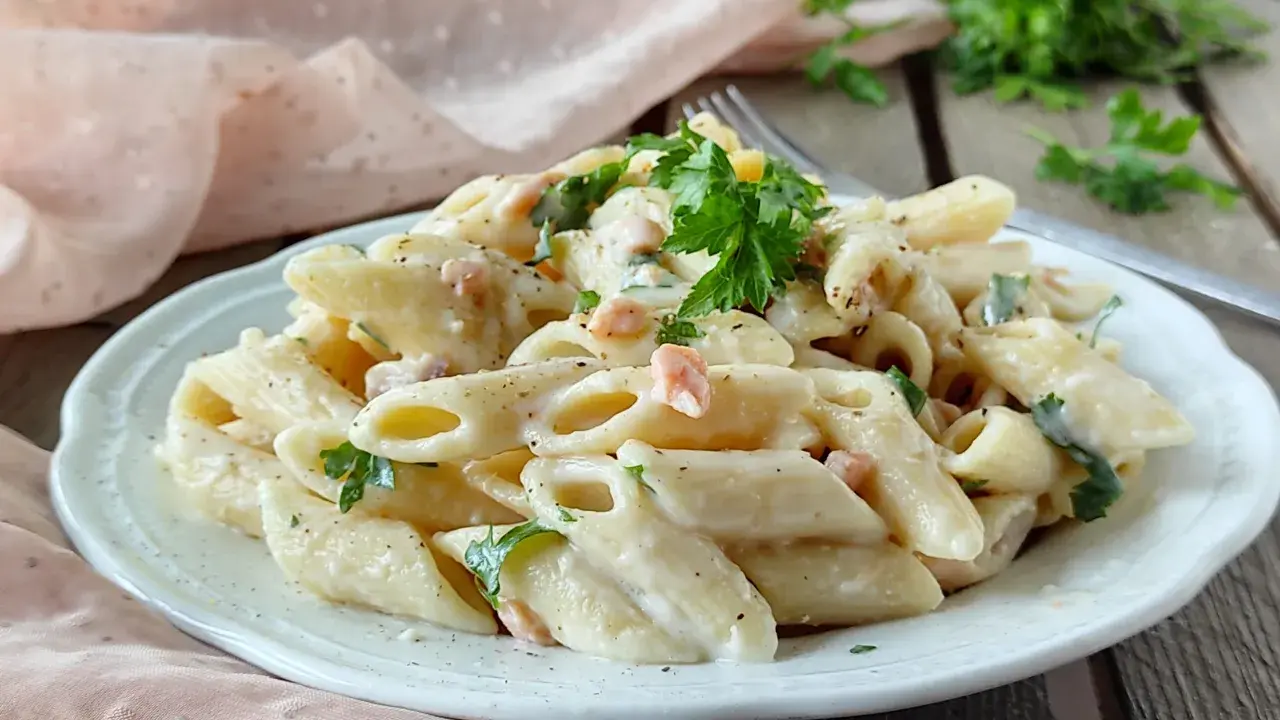Piatto di pasta panna e salmone, guarnito con prezzemolo fresco, servito su un piatto bianco.
