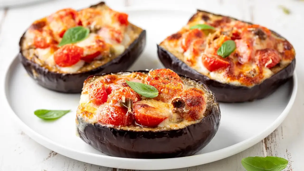 Melanzane ripiene vegetariane, gustose e colorate, con pomodorini e formaggio filante, guarnite con basilico fresco.