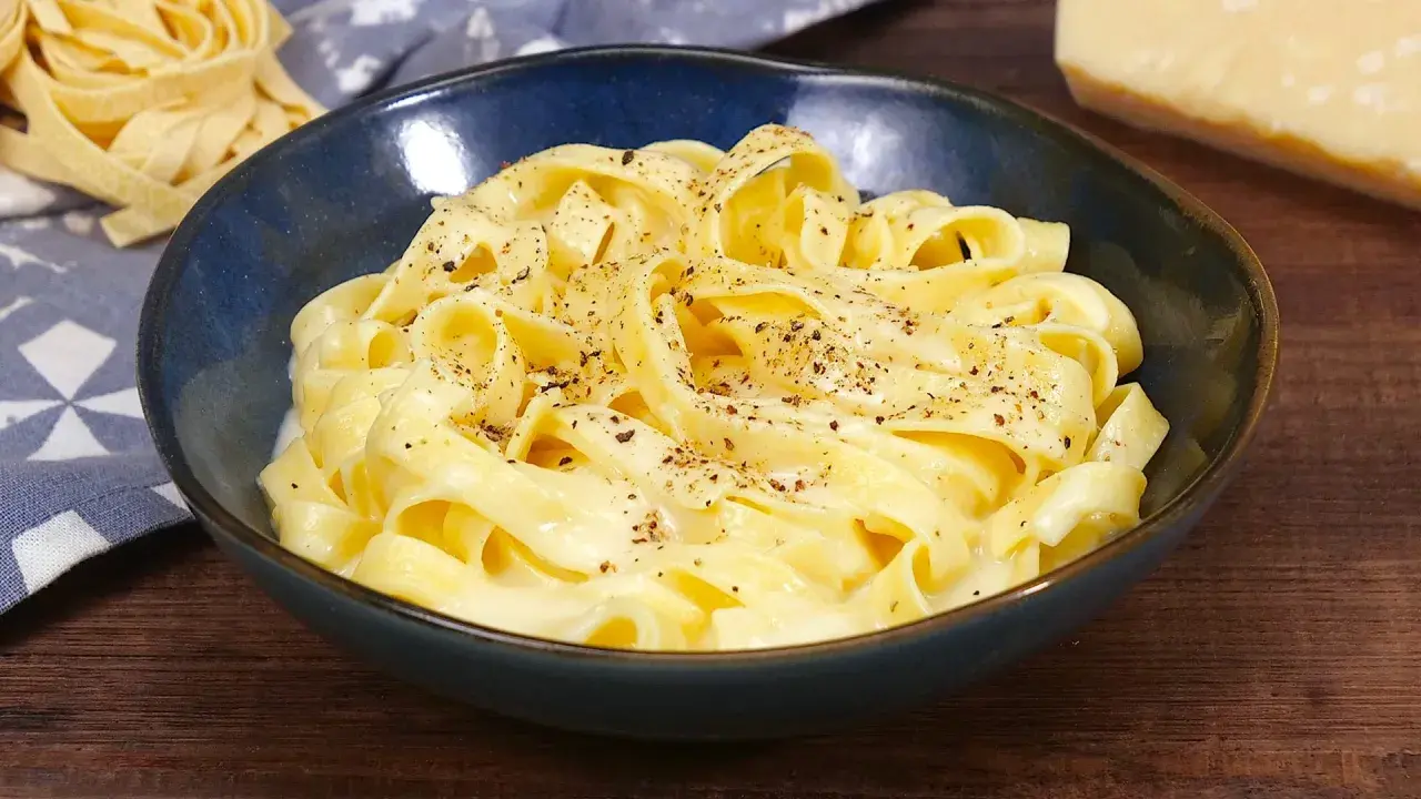 Un piatto di fettuccine alfredo fumanti, condite con una cremosa salsa al parmigiano e pepe nero.