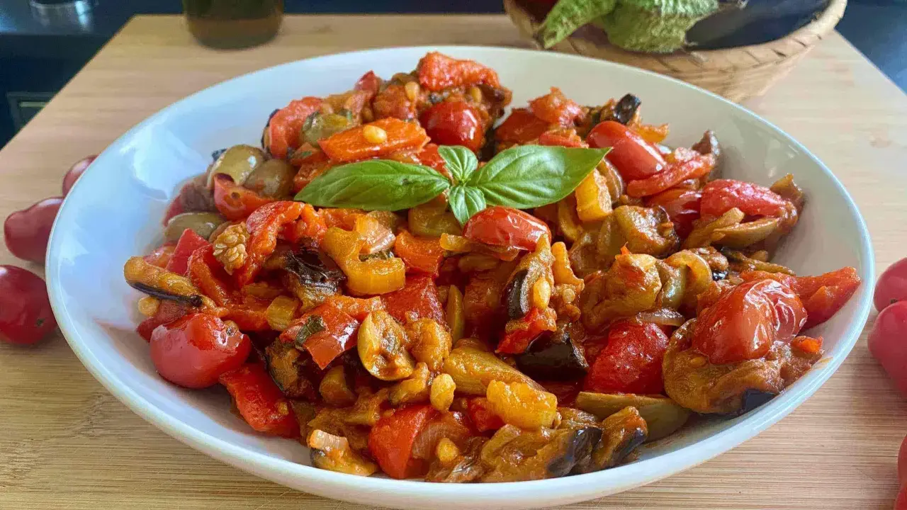 Caponata siciliana ricetta della nonna: un piatto colorato con melanzane, peperoni, pomodorini e basilico, pronto per essere gustato.