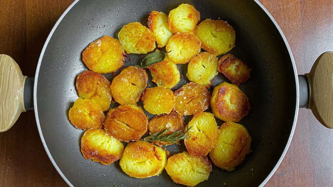 Patate dorate e croccanti in padella, pronte per deliziose ricette con patate. Un rametto di rosmarino aggiunge profumo.