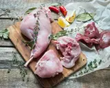 Coniglio crudo a pezzi su tagliere di legno, con erbe aromatiche, limone e peperoncino. Perfetto per un vino da abbinare al coniglio.