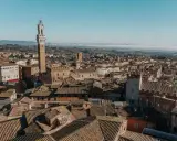 Vista aerea di Siena, con la Torre del Mangia in primo piano. Un'idea per cosa vedere in Toscana in 2 giorni, tra tetti in cotto e colline nebbiose.