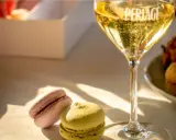 Un bicchiere di spumante frizzante, due macarons colorati e una scatola bianca. Un perfetto abbinamento cibo vino per un momento di dolcezza.