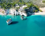 Scogliere bianche a picco sul mare turchese, con rocce isolate e vegetazione lussureggiante. Sembra la spiaggia più bella della Puglia.