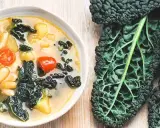 Zuppa ricca con fagioli, pomodoro e il sapore intenso del cavolo nero. Accanto, una foglia di cavolo nero fresca.