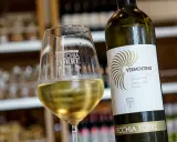 Un bicchiere di vino bianco Vermentino, frizzante e dorato, accanto alla sua bottiglia Vecchia Torre.
