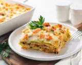 Una fetta di lasagne di pesce, stratificata con salmone e zucchine, guarnita con prezzemolo.