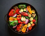 Un assortimento colorato di verdure grigliate, tra cui peperoni, zucchine, cipolle rosse e pomodorini, disposte in una padella di ghisa.