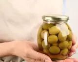 Mani che tengono un barattolo di olive verdi in salamoia per olive, pronte per essere gustate.