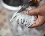 Mano che taglia con un coltello i tentacoli di una seppia, parte del processo per pulire le seppie.