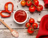 Un ciotola di ketchup fatto in casa, pomodori freschi, peperone rosso, aglio e sale rosa su un tavolo di legno.
