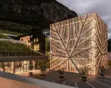 Cantina Sociale Bolzano: edificio moderno con facciata luminosa a forma di foglia, circondato da vigneti e montagne.