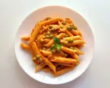 Penne ai 7 peccati: un piatto di pasta cremosa con piselli e un tocco di pomodoro, guarnito con prezzemolo fresco.