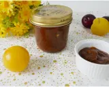 Vasetto di marmellata di susine fatto in casa, con prugne rosse e gialle e fiori gialli sullo sfondo.