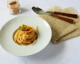 Spaghetti alla bottarga, un piatto semplice ma gustoso, pronto per essere assaporato. Un vasetto di bottarga in polvere e posate completano la scena.