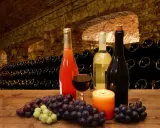 Uva e bottiglie di vino in una cantina storica, con un bicchiere di rosso e una candela. I vitigni Franciacorta sono pronti per essere degustati.