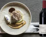 Piatto gourmet con carne, cereali e salsa, accanto a una bottiglia di Lagrein Riserva. Perfetti lagrein abbinamenti per un'esperienza culinaria raffinata.