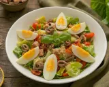 Insalata nizzarda con uova sode, tonno, acciughe, pomodorini e lattuga. Ingredienti freschi per un piatto gustoso.